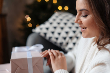 Woman in cozy setting opening a gift box with a ribbon.の写真素材