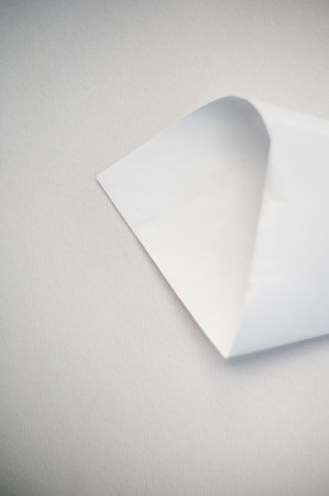 A single sheet of white paper with a folded corner on a textured surface.の写真素材