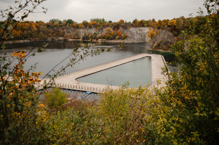 A triangular pier extends into a calm lake surrounded by autumn foliage.の写真素材