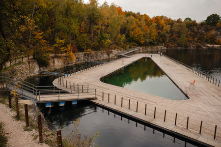 Triangular wooden platform over a lake surrounded by autumn trees. Zakrzowek, Krakow