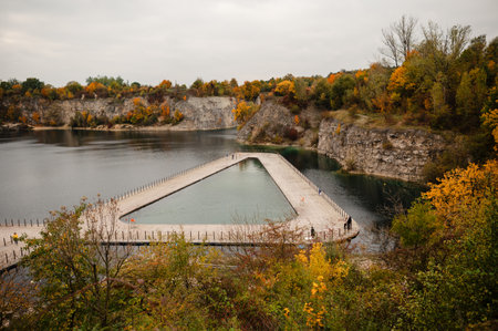 A scenic view of a quarry lake with a unique triangular swimming pool surrounded by autumn foliage.