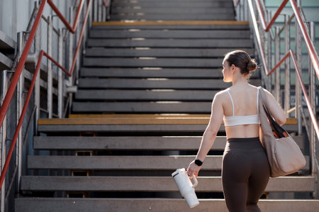 Cute woman walking up stairs carrying a water bottle and a bag, wearing athletic clothingの写真素材