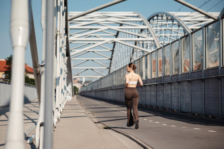 Sporty woman jogging on a modern bridge in urban setting at suuny dayの写真素材