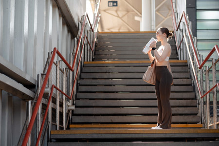 Attractive woman in workout attire drinking from a bottle on stairs at sunny dayの写真素材