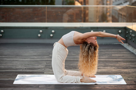 Blonde woman with long curly hair practicing yoga on a rooftop, performing a camel pose.