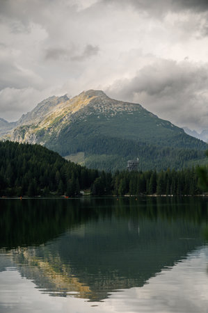 Serene mountain landscape with a lake and forest under cloudy sky. Strbske Pleso Lake, Slovakia