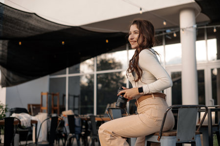 Smiling woman sitting outdoors holding a camera, modern setting.の写真素材