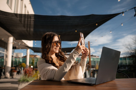 Woman taking a selfie outdoors with a laptop on the table.の写真素材