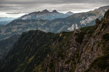 A panoramic view of rugged mountains under a cloudy sky, showcasing steep cliffs and lush green valleysの写真素材