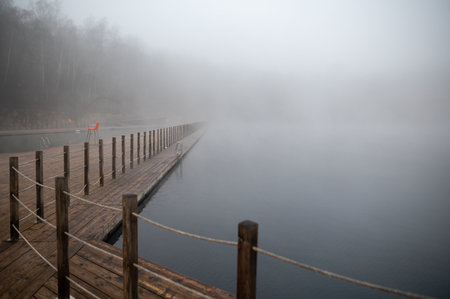 Foggy lake with a wooden pier extending into the mist.の写真素材