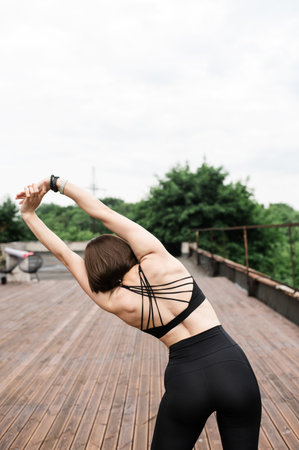 Back view of strong sporty woman with short hair stretching outdoors on a wooden deck with trees in background.の写真素材