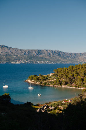 A scenic view of a tranquil bay on the Dalmatian Coast, Croatia, dotted with sailboats and surrounded by lush green hills and distant mountainsの写真素材