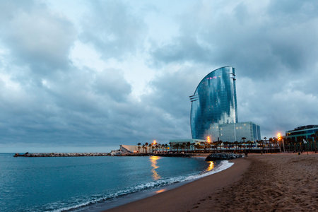 The modern sail-shaped building stands prominently on the Barceloneta beach as twilight descends,...