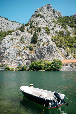 A small boat floats on the emerald waters of the Cetina River near Omis, Croatia, with a tunnel...