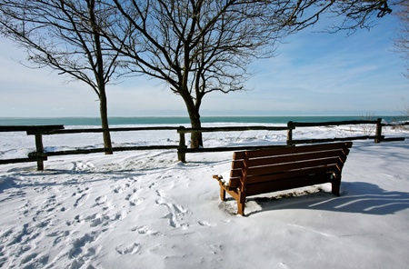 a winter scene of a snow-covered bench overlooking the lakeの写真素材