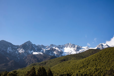 Mountain landscape with snow-capped peaks, forest and blue skyの写真素材