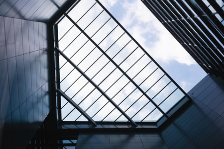 Low angle view of modern office building with glass roof and blue skyの写真素材