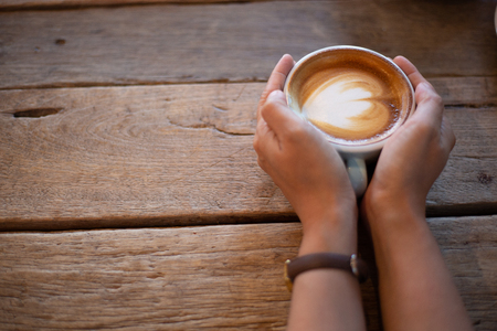 Hand Women put a Latte arts coffe hot coffee on wooden table.barista art concept.の写真素材