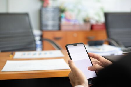businessman hands searching for data on moblie phone with analyzing charts at his workplace.