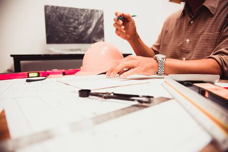 Architect calculating structure estimates in blueprint at Construction Site With drawing...