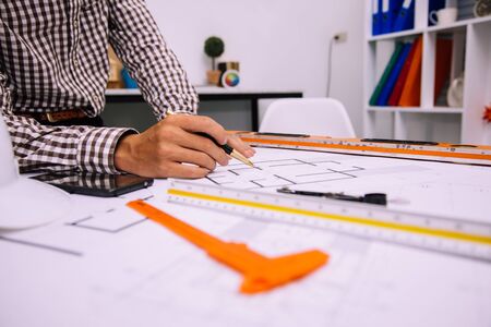 Close-up hand of male Architect drawing blueprint on work space in construction site.