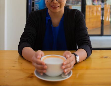 Hand Women put a Latte arts coffe hot coffee on wooden table.barista love art concept.の写真素材