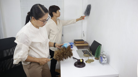 Two women are cleaning an office together.white office environment, showing teamwork and attention...