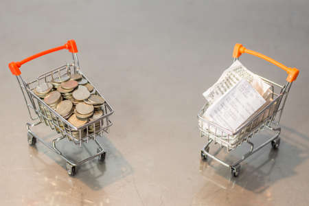 Close up coins and receipts paper on mini shopping cart with natural light background (Business and finance concept)の写真素材