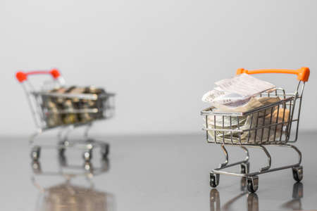 Close up coins and receipts paper on mini shopping cart with natural light background (Business and finance concept)の写真素材