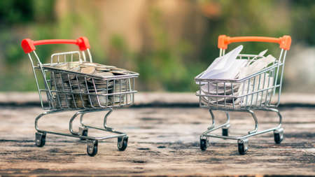 Close up coins and receipts paper on mini shopping cart with natural light background (Business and finance concept)の写真素材
