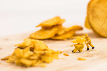 Miniature people, Workers work on  production potato chips on white background (food concept)