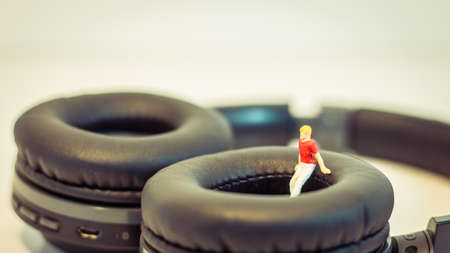 Miniature people, Young man sitting on headphone on white background (Alone music concept)の写真素材