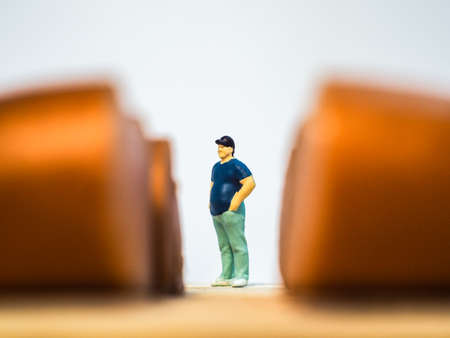 Miniature people : Close up fat man standing and looking at sausages isolated on white background (Food concept)の写真素材