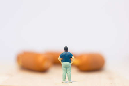 Miniature people : Close up fat man standing and looking at sausages isolated on white background (Food concept)の写真素材