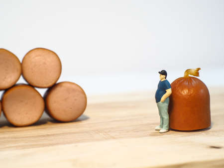 Miniature people : Close up fat man standing and looking at sausages isolated on white background (Food concept)の写真素材