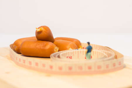 Miniature people : Close up fat man standing and looking at sausages isolated on white background (Food concept)の写真素材