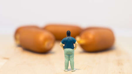 Miniature people : Close up fat man standing and looking at sausages isolated on white background (Food concept)の写真素材