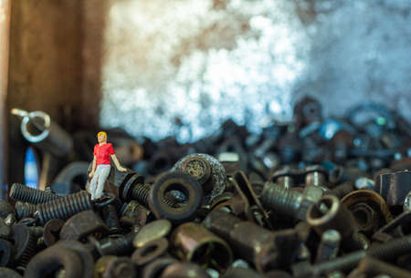Miniature people, Young man sitting on pile of old screws nuts and boltsの写真素材
