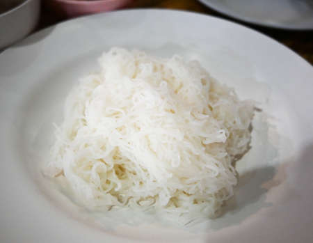 Thai vermicelli (Khanom Chin or slightly fermented noodles) served on a white plate with a spoon and...