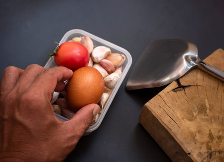 selective focus of hand held eggs with tomatoes and garlic in a container on dark backgroundの写真素材