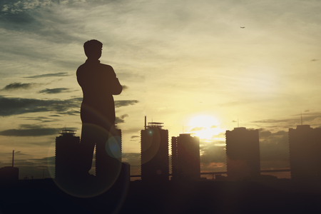 Silhouette of Businessman standing on roof top  looking cityscape at sunset. business target and success concept.の写真素材