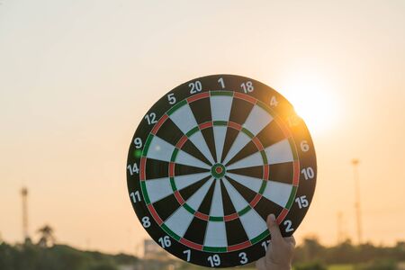 Close up hand holding dartboard on sunset background. Business targeting and focus concept.の写真素材