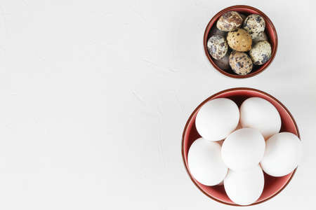 Egg concept for Easter - quail eggs and chicken eggs in bowls on a white table