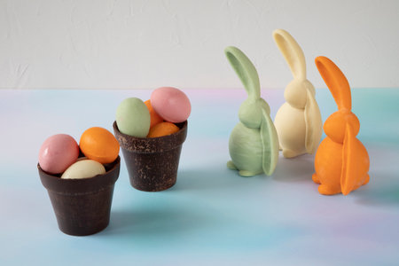 Colorful chocolate bunnies stand near flower pots made of chocolate with an unusual texture with...