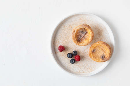 Dessert from Portugal - pastry Pastel de nata from egg custard tart pastry, sprinkled with ground cinnamon and powdered sugar on a plate with blueberries and raspberries - top view and copy spaceの写真素材