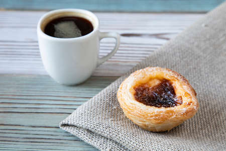 Traditional dessert in Portugal - Pastel de nata cake on textiles on a wooden table with a cup of hot black coffee in a white ceramic - side viewの写真素材