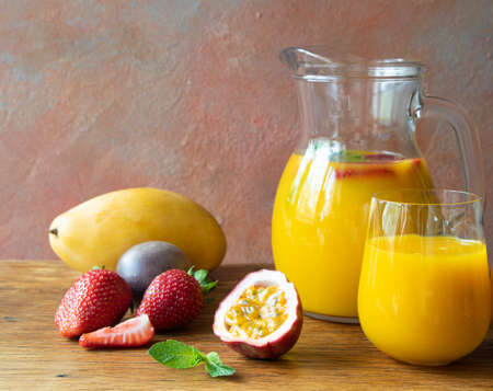 Jug and glass with tropical refreshing cocktail with mango, strawberry, mango, and passion fruit on the wooden table of the cafe with copy space and close-upの写真素材