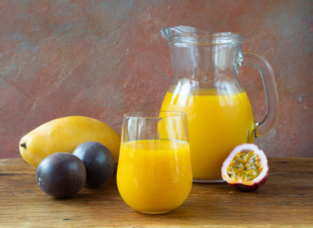 A refreshing yellow drink. The cocktail consists of mango juice, passion fruit, and citrus fruits: orange and lemon in a glass jug and a glass on a wooden tableの写真素材