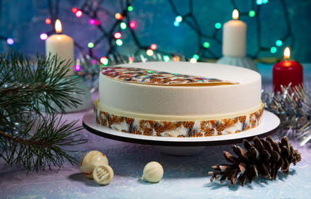 Festive New Year's cake for Christmas or Christmas Eve with beautiful decorations on a winter background with burning candles and a garland with colorful lightsの写真素材