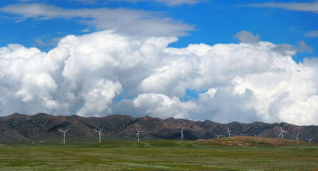 Landscape Of Wind turbines Or Windmills On Green Grass Fields With Mountain Ranges And Cloudy Blue...